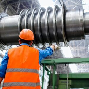 Engineer in high visibility vest and hard hat inspecting large machinery in factory setting.
